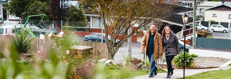 Photo of a man and woman, hand in hand walking up a garden path toward the camera. The house is behind the camera.