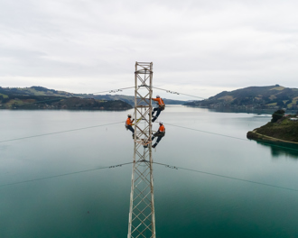 Three workers on a tower with the Otago Harbour in the background