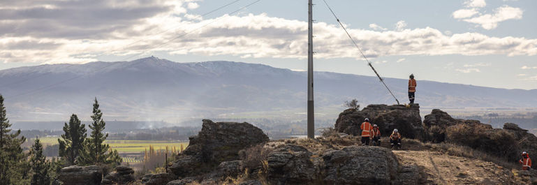Photo of Earnscleugh Rd lines project, workers standing next to a power pole atop a dusty and rocky hill.
