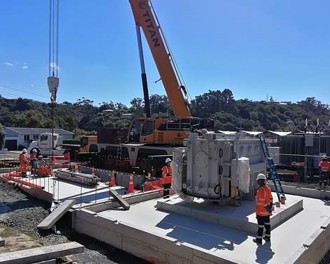 Photo shows transformer in place on concrete foundations. Crane in background and clear blue skies.
