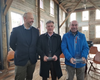 Three men standing in front of camera at afternoon tea on Quarantine Island Kamau Taurua, two of them are holding glass awards.