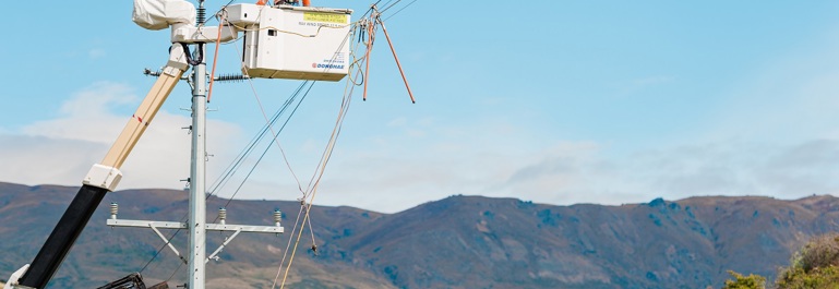 Photo of a worker in a cherry picker basket lifted to the top of a power pole. Power lines haave been clipped together to allow work to progress safely.