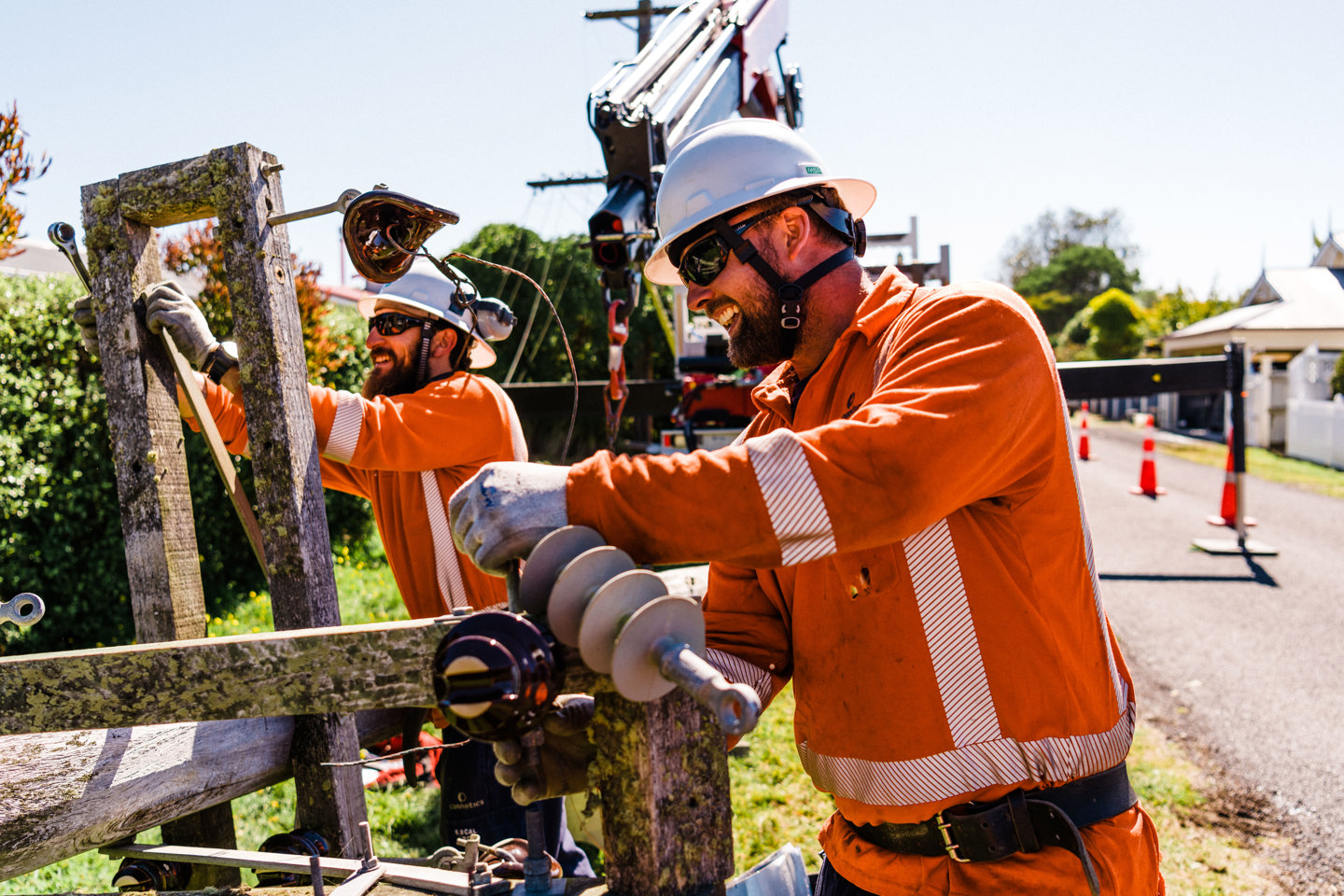 A photo of two contractors working on a power pole that is lying on the ground.