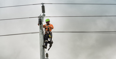 Worker in a safety harness working on the top of a power pole.