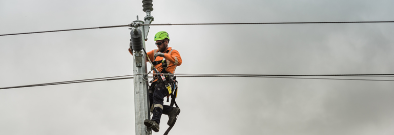 Worker in a safety harness working on the top of a power pole.