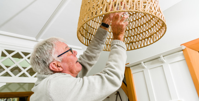 Photo of an older man reaching up to change a lightbulb.