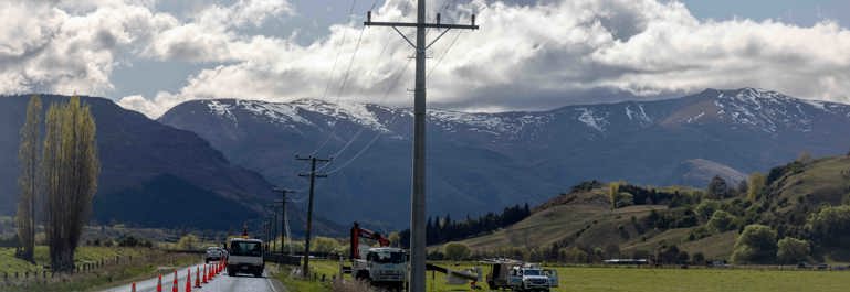 Photo showing utility trucks alongside powerlines. Rural setting with mountains in the background