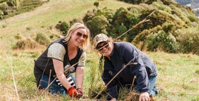 Aurora Energy Planting Day, two women kneeling down planting natives trees.