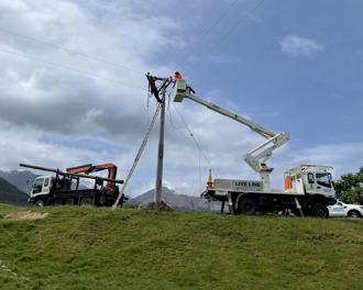 Photo shows two Delta trucks and a ute, one of the trucks has a cherry picker with a person in the basket who has been lifted to the top of a power pole.