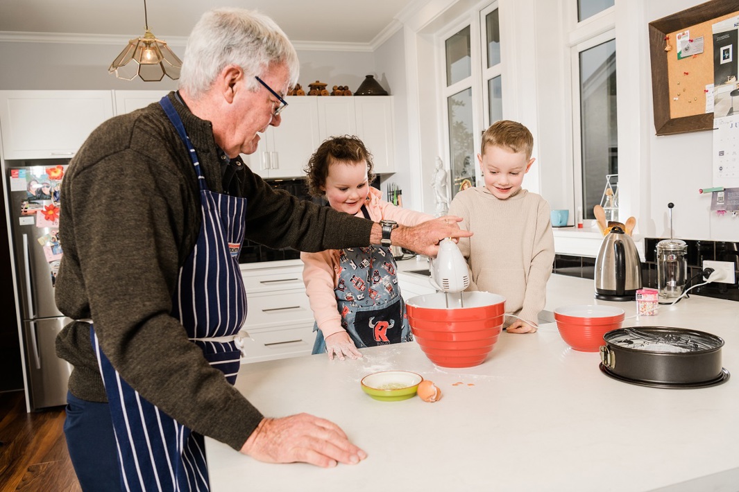 Elderly man in the kitchen helping two young children with baking