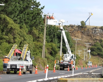 Photo shows three power poles along of stretch of terrain being worked on simultaneously with works in three separate cherry pickers.