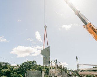 Photo of crane lifting prefabricated concrete into place at the Andy Bay substation upgrade construction site. The sun is shining behind the crane's arm.
