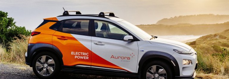 Photo of Aurora Energy branded electric car with the sun setting in the background.
