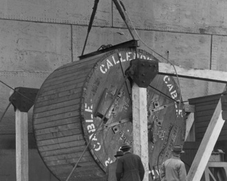 1947, a large reel holding the original submarine electricity cable for Otago Harbour next to a ship and three men inspecting it